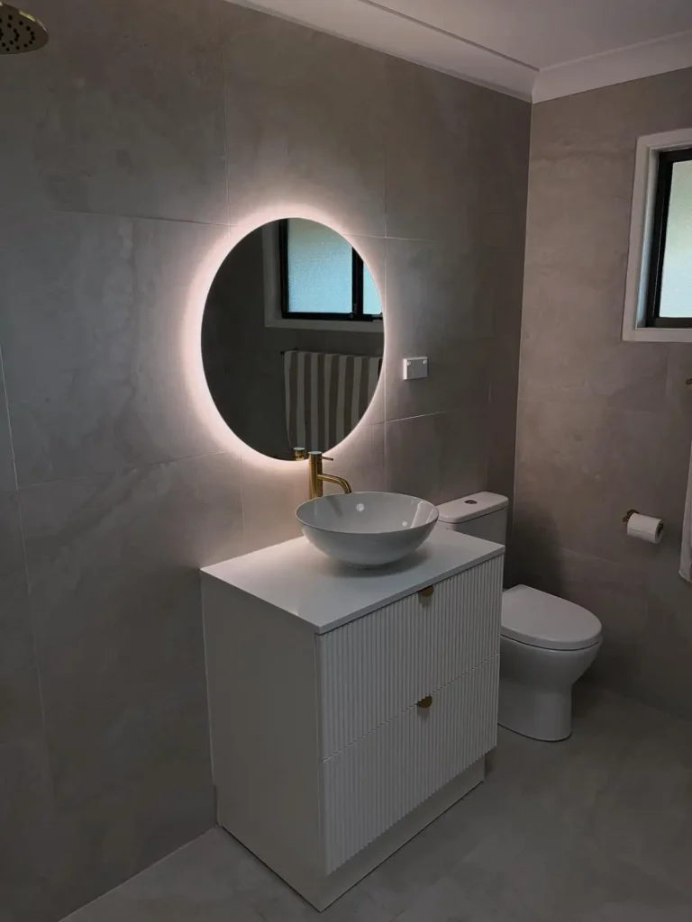 Modern bathroom vanity with round LED backlit mirror and feature lighting